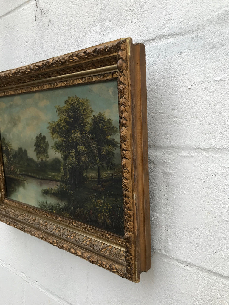 A very old antique painting on canvas of a body of water and trees and blue skies. Beautiful thick gold gesso wood frame.  Some pieces of the exterior gesso face have come off and they have been touched up with gold paint. Width: 22,  Height: 16 inch