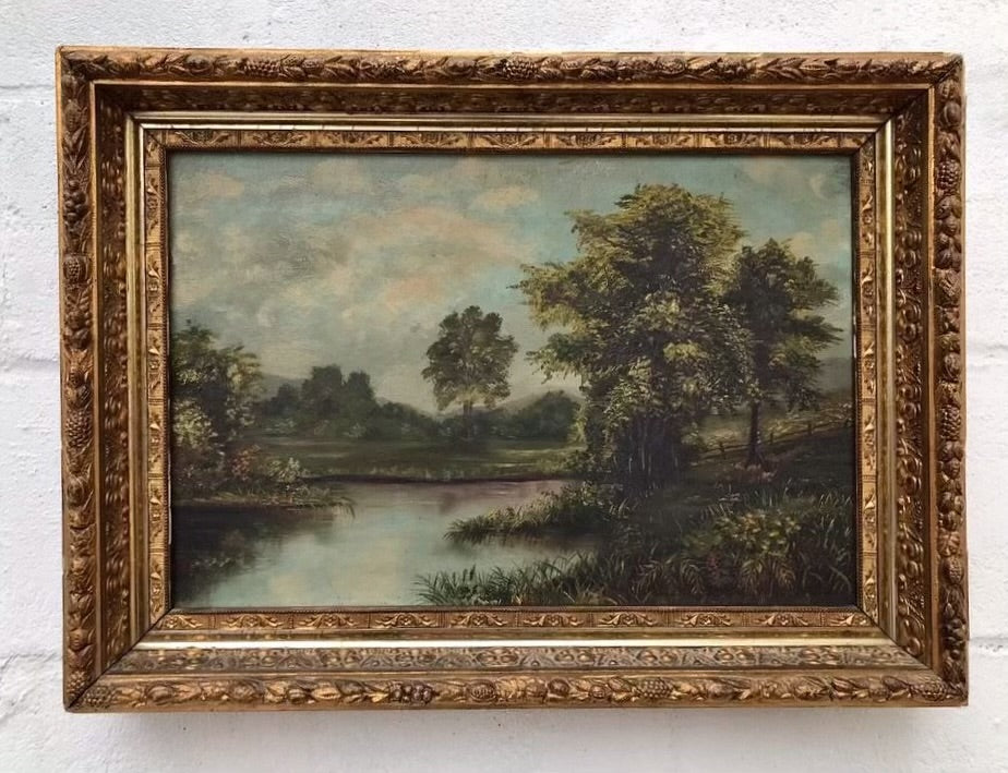 A very old antique painting on canvas of a body of water and trees and blue skies. Beautiful thick gold gesso wood frame.  Some pieces of the exterior gesso face have come off and they have been touched up with gold paint. Width: 22,  Height: 16 inch
